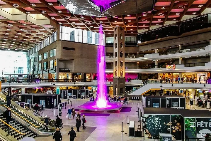 Large shopping mall atrium with a tall purple illuminated fountain